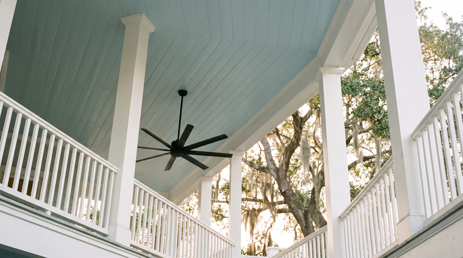 A pale haint blue beadboard porch ceiling with white columns and a ceiling fan
